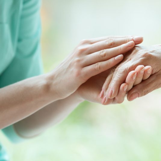 Young caretaker massaging pensioner's hand with Parkinson's disease